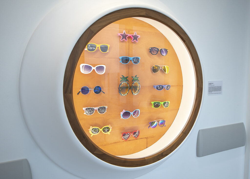 several pairs of sunglasses in a large round display case with a round window