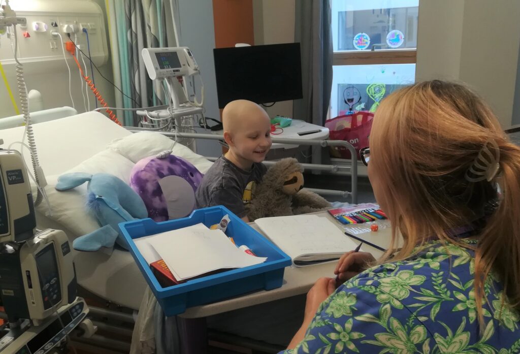 a nurse sitting beside a child in a hospital bed using an over bed table to colour in