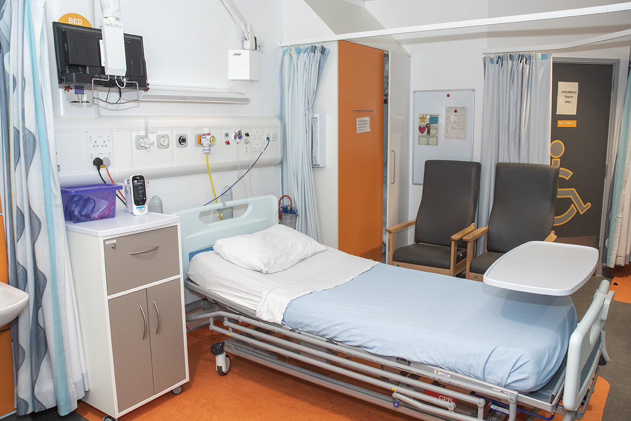 a hospital single bed with a disabled toilet and two chairs near it