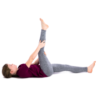 A person is lying on their back on the floor, lifting one leg straight up in the air while holding it with both hands. The other leg is extended flat on the ground. This appears to be a hamstring stretch.
