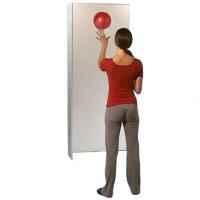 A woman wearing a red top and grey trousers bouncing a red ball off of a grey wall to catch it
