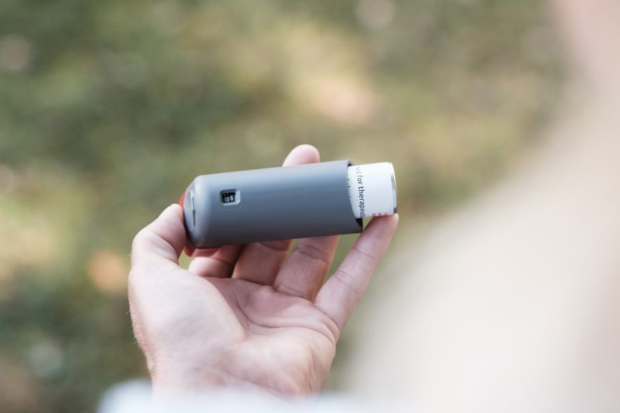Close-up of a hand holding a grey inhaler in a natural outdoor setting