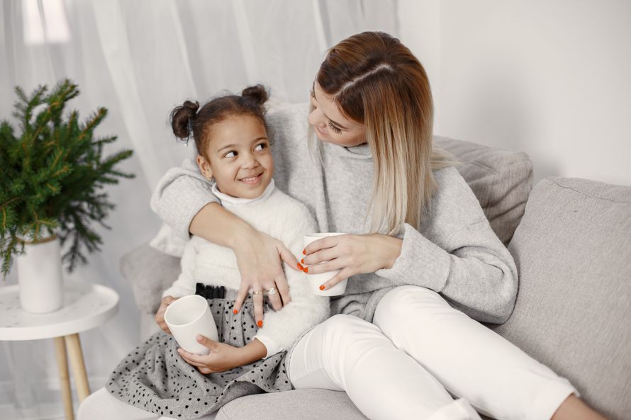 A mother and daughter enjoy cozy time together with hot drinks on a sofa