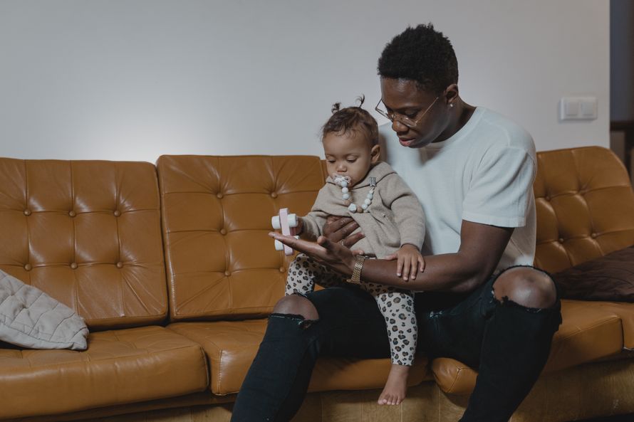 A father lovingly holds his baby on a leather sofa and showing them a toy car